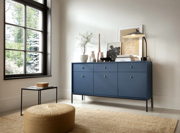 Szeroka komoda granatowa Mono MKSZ154 ustawiona przy ścianie w salonie, na blacie złote dodatki i rośliny, styl navy blue i loft