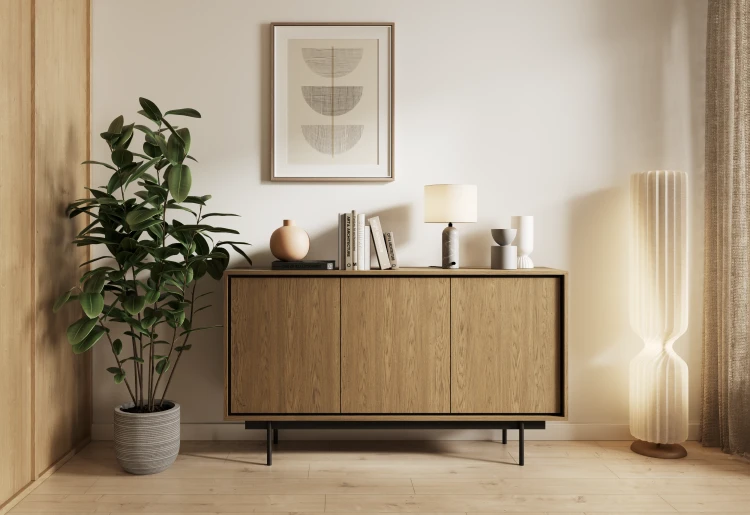 Elegancka komoda Deco K3D w odcieniu Baltic Dune zaaranżowana w nowoczesnym salonie, z dekoracjami postawionymi na blacie i robotem odkurzającym swobodnie przejeżdżającym pod meblem.