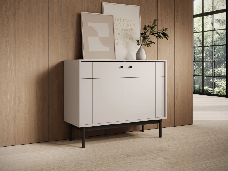 Elegancka komoda Japandi K104 w kolorze kaszmir ustawiona przy gładkiej ścianie, prezentująca smukłe czarne nóżki i nowoczesny design bryły