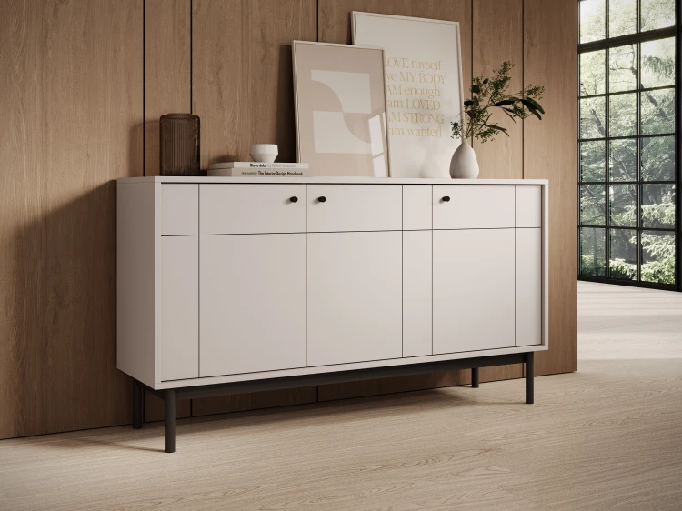 Elegancka komoda Japandi K154 w kolorze kaszmir ustawiona przy gładkiej ścianie, prezentująca smukłe czarne nóżki i nowoczesny design bryły